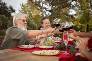 elderly people drinking red wine and eating dinner outdoors