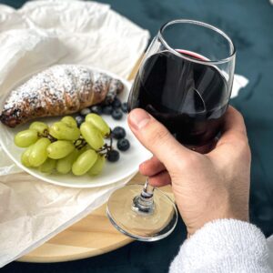 hand holding red wine glass with grapes and scone